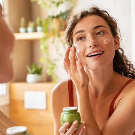 Femme souriante appliquant une crème éclat sur le visage pour raviver son teint en hiver